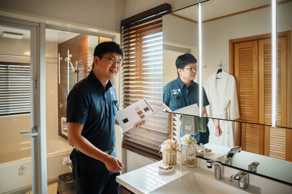 洗面化粧台の前でカタログを手に持ち、設備のポイントを説明する男性スタッフ
