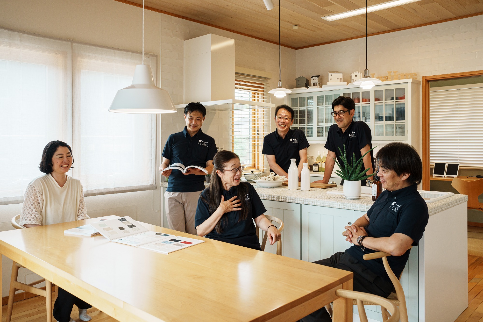 明るいキッチンとダイニングテーブルを囲んで、笑顔で打ち合わせをする住宅会社のスタッフたち